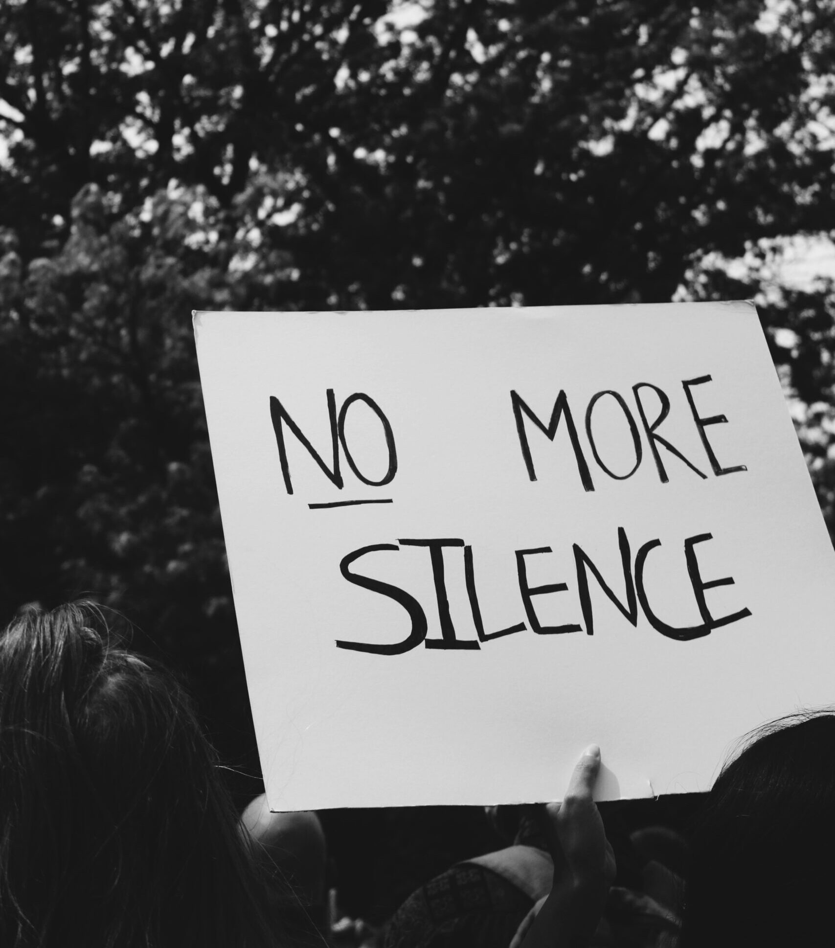 immagine BN di una manifestazione. un cartello con scritto: no more silence