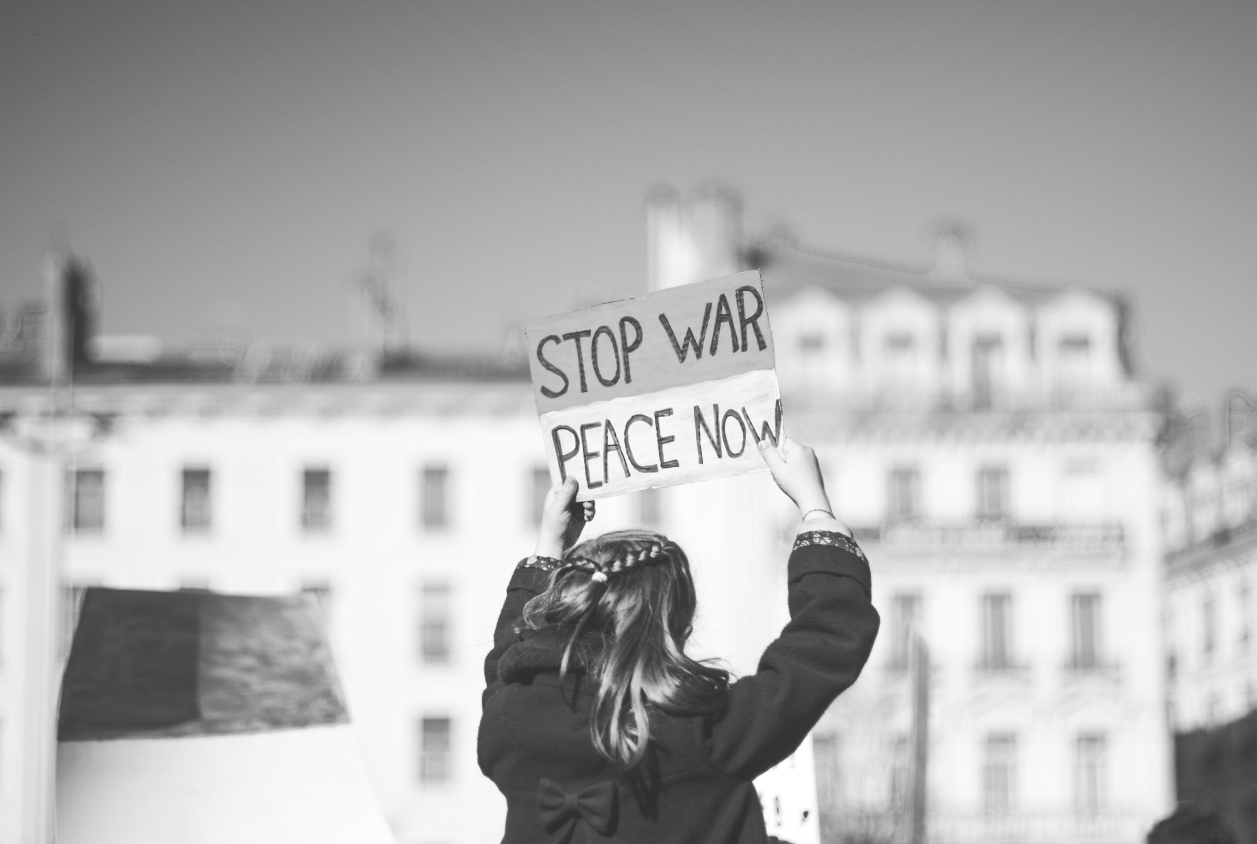 una bambina di spalle con un cartello: stop war peace now