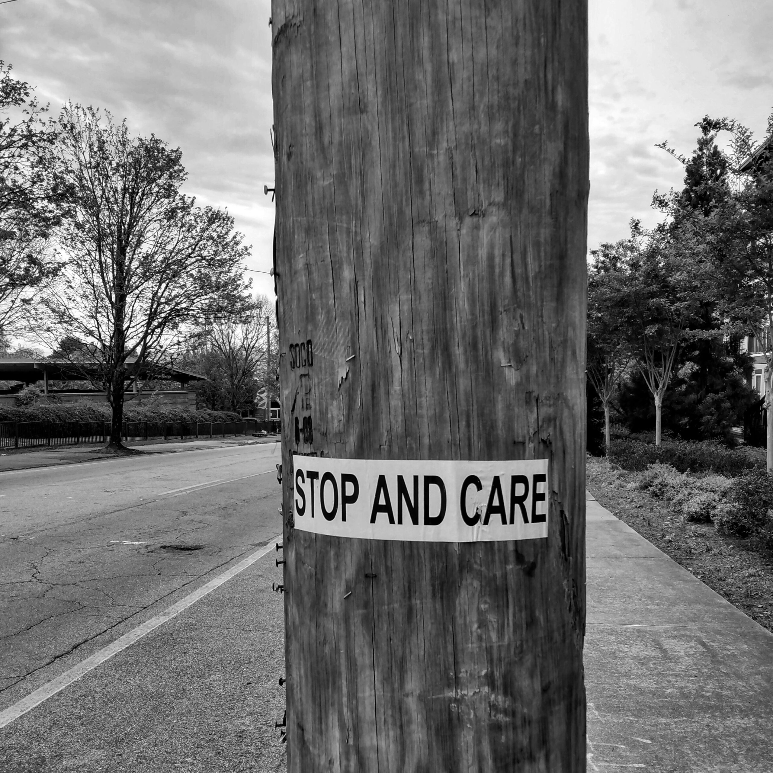 foto bn di un palo in legno con scritto stop and care